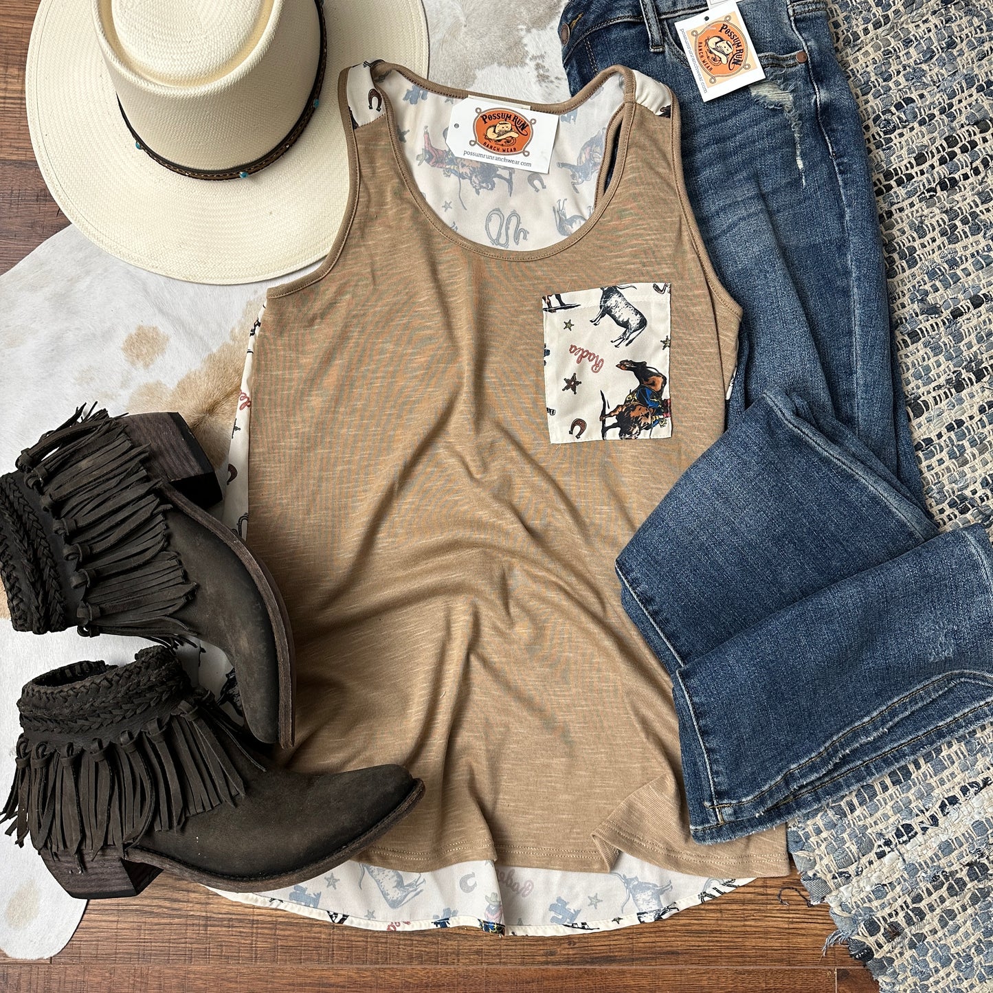 Taupe colored racerback tank that has cowboy printed contrasting front chest pocket and rear panel.