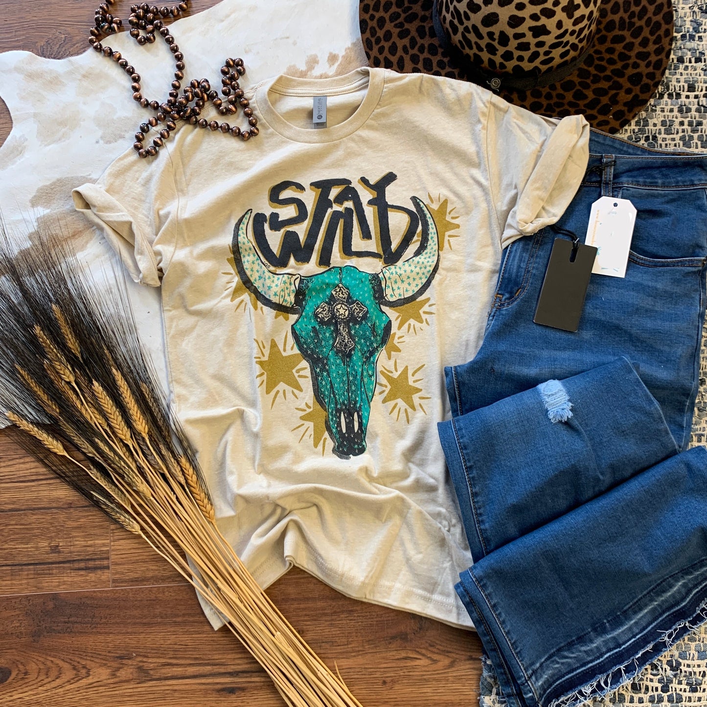 tan graphic tee with turquoise skull that says Stay Wild
