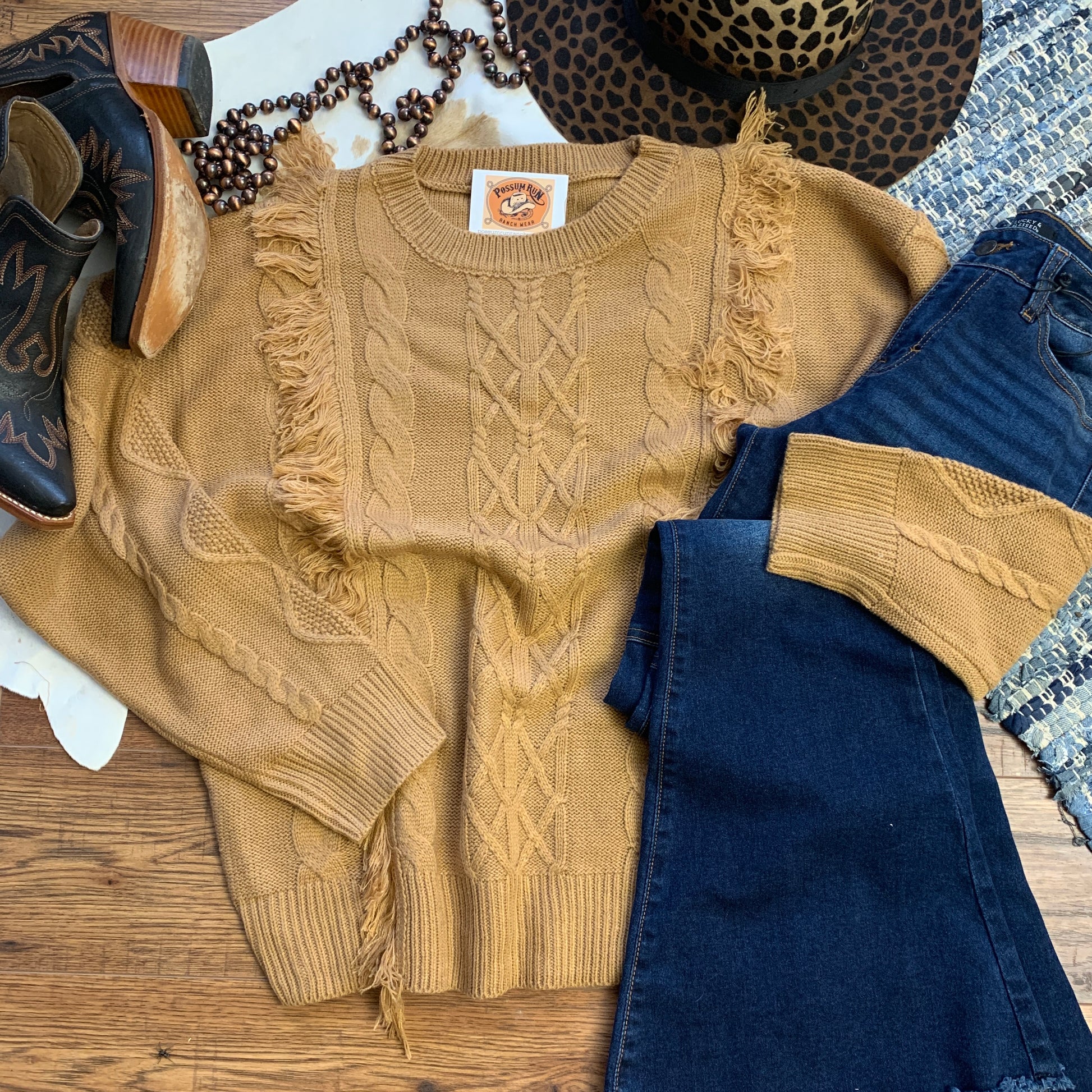 camel/ tan knit sweater with vertical fringe on it, paired with jeans and shoes.